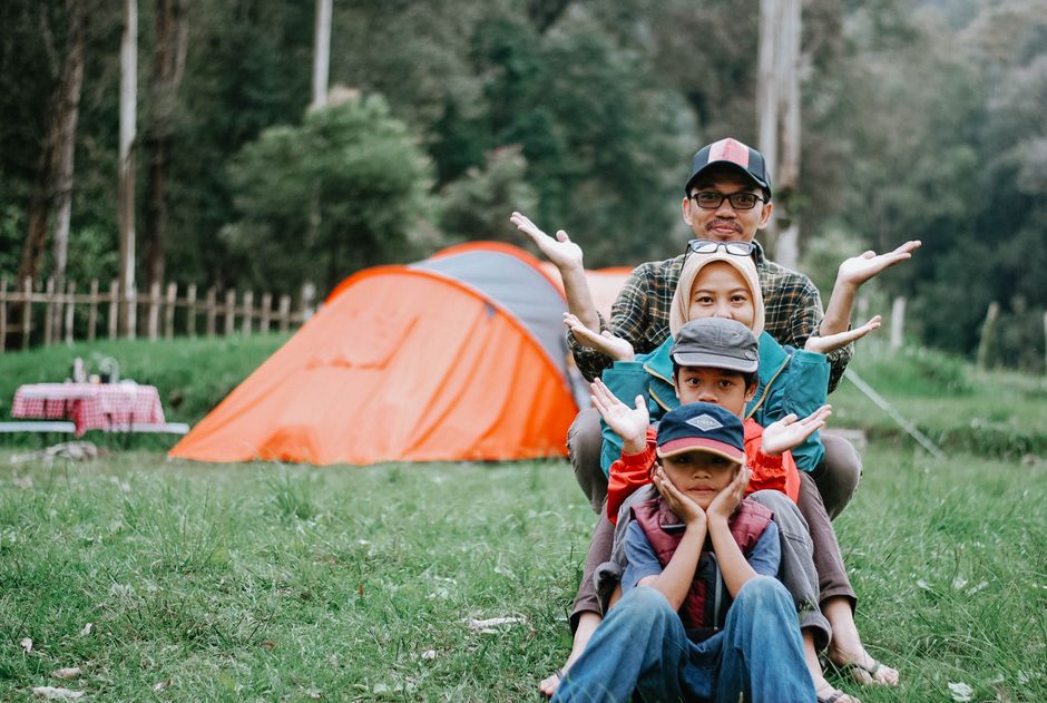 Family enjoying a fun camping trip with colorful tent in a lush green landscape.